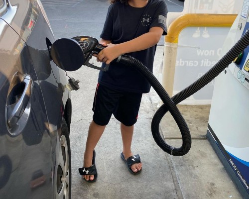 A young boy examining economic implications while filling up his car at a gas station.